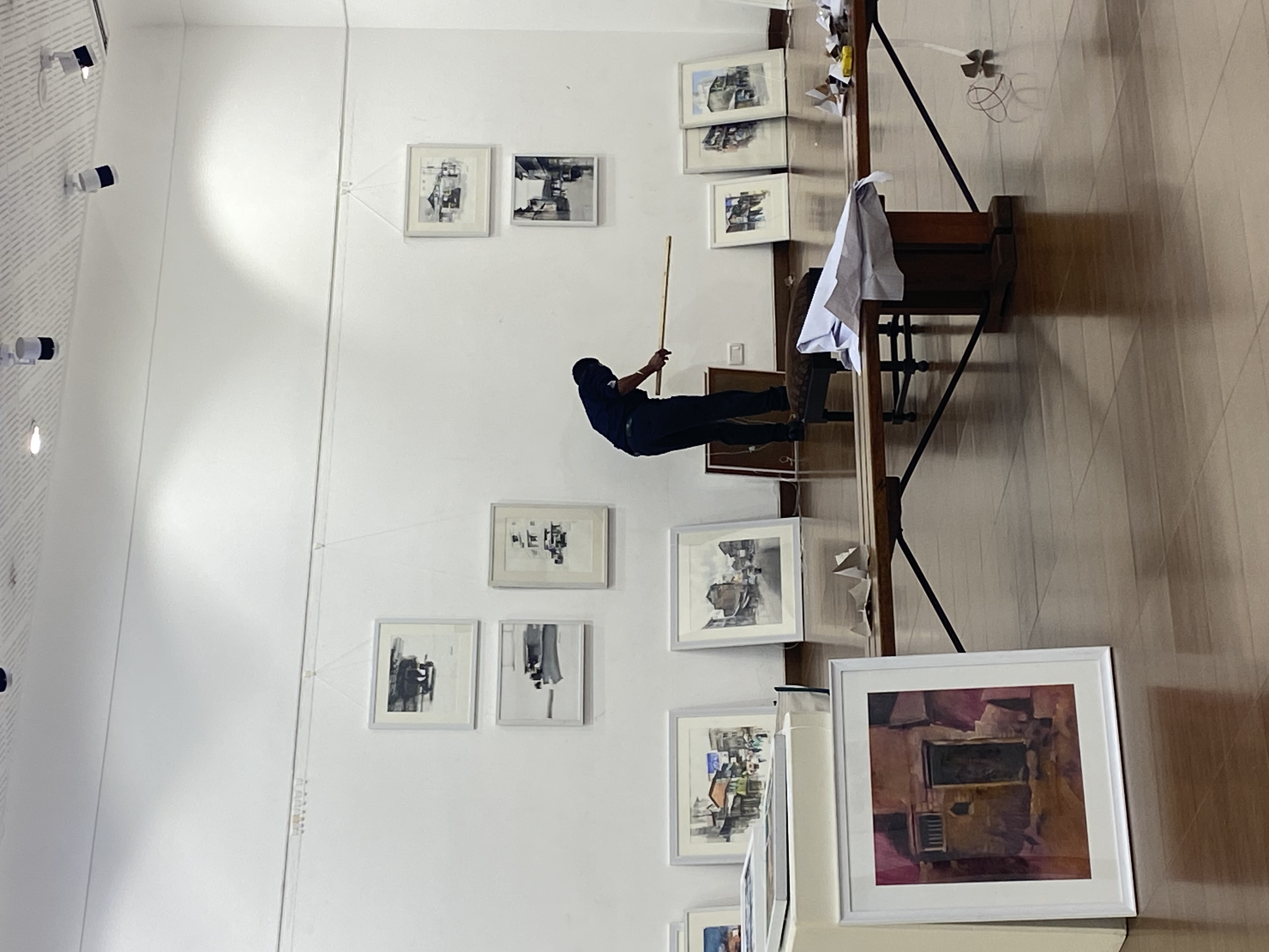 Install in progress - a gallery hand measures the hang while framed watercolours wait along the wall