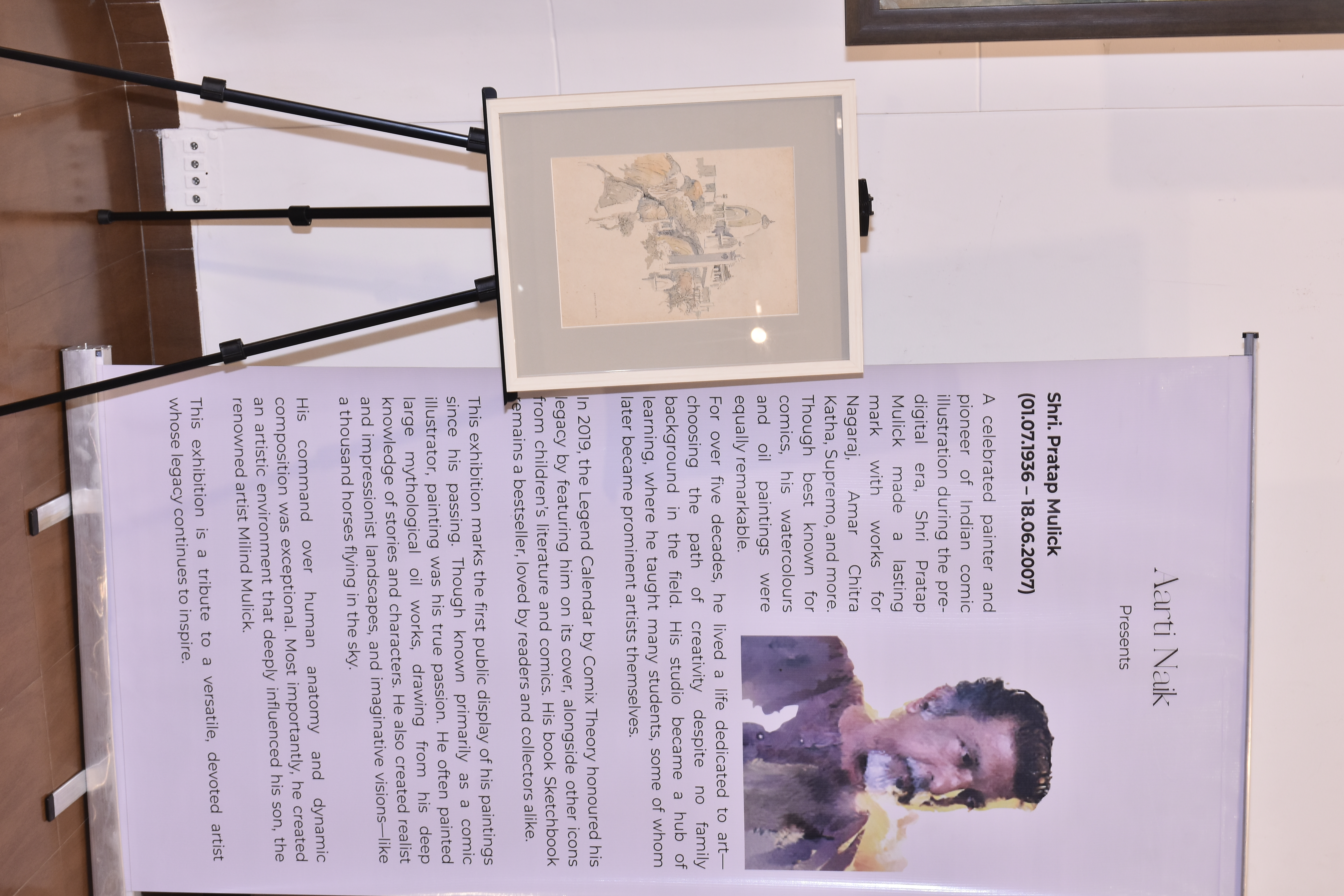 The About Pratap Mulick standee beside a framed pencil sketch on an easel